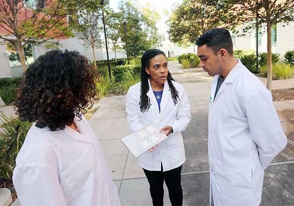 Professor Foster speaking to one male student and one female student wearing lab coats
